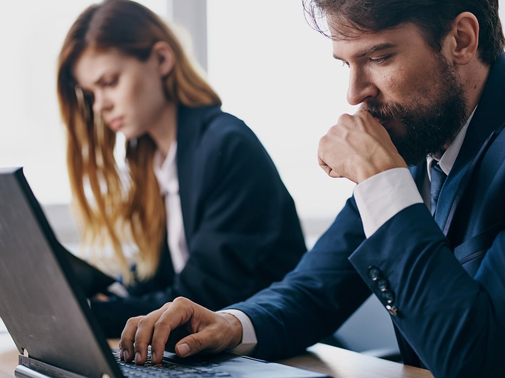 Business professionals in suits looking concerned while working on laptops during a manual supplier registration process for every project