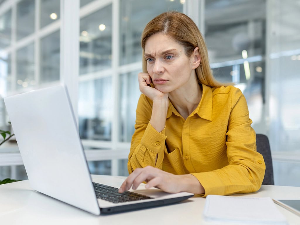 Businesswoman in an office looking concerned at her laptop while dealing with a manual supplier registration process for multiple projects